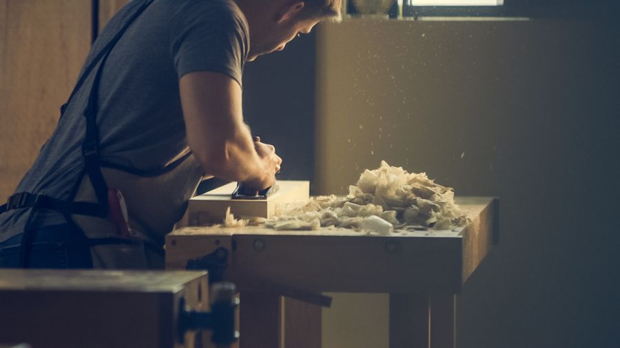 Pengrajin membentuk kayu di meja kerja dengan serutan kayu